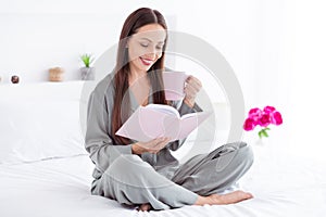 Photo of cheerful cute lady wear grey pajama enjoy weekend drinking tea reading book indoors house bedroom