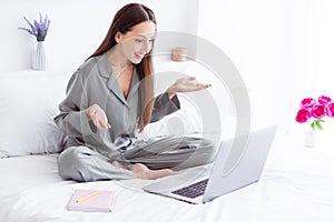 Photo of cheerful cute lady wear grey pajama talking modern device sititng bed indoors house bedroom