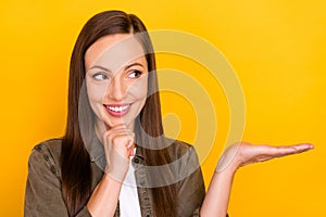 Photo of cheerful dreamy young woman hold hand empty space look idea isolated on yellow color background