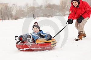 Photo of cheerful father skating son on tubing in winter afternoon