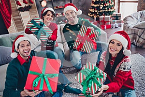 Photo of cheerful funky buddies sit sofa floor hold desirable christmas festive giftbox apartment inside