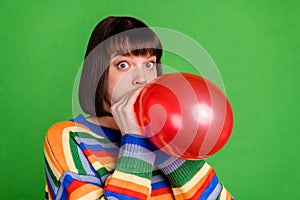 Photo of cheerful funky childish young woman hold hands balloon blow air isolated on green color background