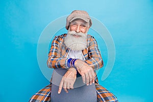 Photo of cheerful funky retired man dressed plaid suit smiling sitting chair isolated blue color background