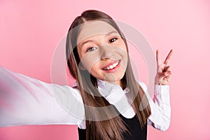 Photo of cheerful happy positive young small girl good mood v-sign make selfie  on pink color background