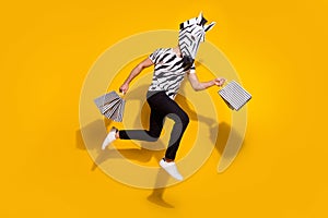 Photo of cheerful hurrying man wear zebra print t-shirt mask holding shoppers running fast jumping high isolated yellow