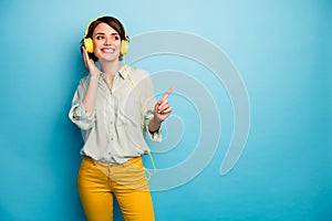 Photo of cheerful lady listen radio stylish earphones raise finger indicating empty space wear casual green shirt yellow photo