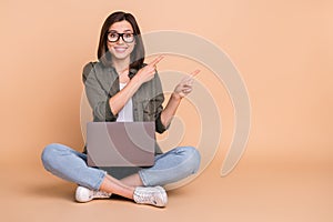 Photo of cheerful lady sit floor hold pc indicate finger empty space sale wear khaki shirt  beige color