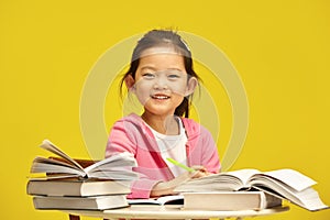 Photo of cheerful little Asian ethnicity first grader schoolgirl enjoying her reading time with books, happy smiling