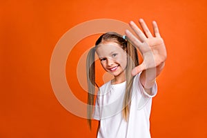 Photo of cheerful lovely girl toothy smile arm palm waving hi empty space isolated on orange color background