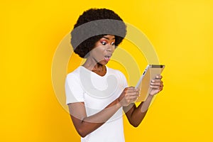 Photo of cheerful nice amazed dark skin young woman look tablet isolated on yellow color background