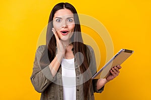 Photo of cheerful nice young amazed shocked woman hold hand cheek tablet isolated on yellow color background