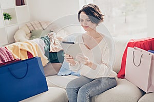 Photo of cheerful nice young woman sit sofa look hold tablet order shopping online bags indoors on house living room
