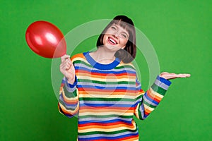 Photo of cheerful nice young woman smile hold hands empty space balloon isolated on green color background