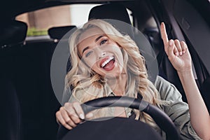 Photo of cheerful overjoyed person sitting driver seat hold wheel point finger enjoy radio station