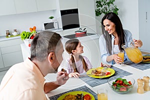 Photo of cheerful parents communicate pour fresh juice small daughter domestic food plate serenity house kitchen inside