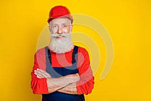 Photo of cheerful positive age man workwear overall red hard hat arms folded empty space isolated yellow color