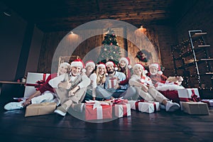 Photo of cheerful positive big family surrounded with gift boxed smiling toothily in front of christmas tree lights