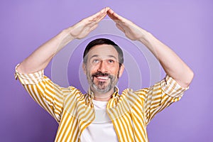 Photo of cheerful positive happy man look above head hands roof house isolated on purple color background