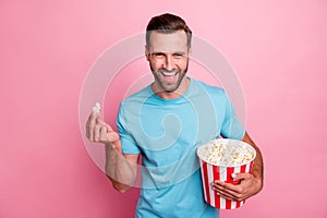 Photo of cheerful positive man watching tv series holding bucket of popcorn tasting smiling toothily comedy isolated in