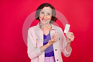 Photo of cheerful positive old grandma demonstrate meds drugs wear pink jacket isolated red color background
