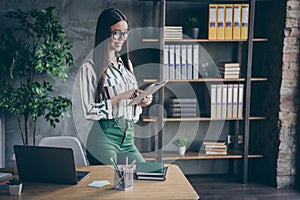 Photo of cheerful positive pretty cute nice woman smiling toothily wearing green pants in spectacles standing by desktop