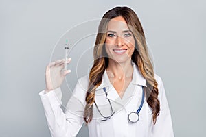 Photo of cheerful positive woman doc dressed white coat holding syringe smiling isolated grey color background