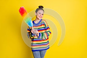 Photo of cheerful pretty young woman stand empty space hold colorful feather cleaner isolated on bright yellow color