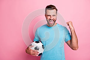 Photo of cheerful shouting handsome man making fist having won important soccer game with ball in hand saying yeah