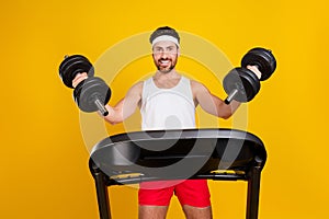 Photo of cheerful strong guy activewear walking treadmill rising dumbbells isolated yellow color background