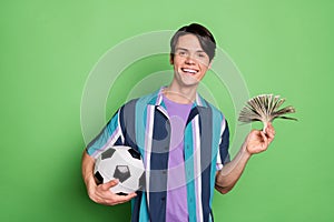 Photo of cheerful young happy positive man hold hands money football bet isolated on green color background