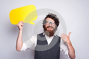 Photo of cheerful young hipster guy holding epmty yellow speech bubble