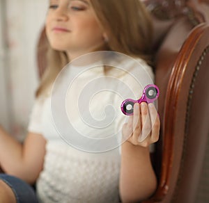 Photo of a child with green and pink fidget spinners in hands, sitting in leather chair, wearing white shirt