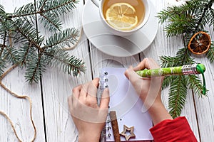 A photo of children`s hands writing in a note book, a cuo of tea anf Christmas decoration