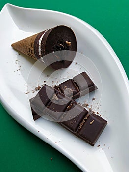 Photo of chocolate ice cream in waffle cones. Served on white plate on green background with dark bitter chocolate