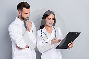 Photo of clever thoughtful two docs dressed white coats reading list clipboard isolated grey color background