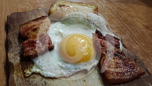 Photo close-up view of fried eggs with slices of fried bacon and croutons