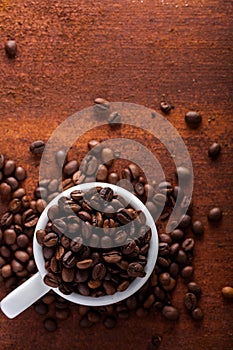 Photo closeup of coffee beans in white cup. Rusty background.