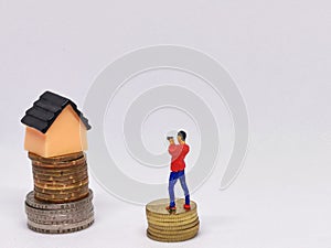 Photo of coins with miniature house and human  on white background.