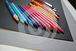 Photo of colored pencils arranged in a color gradient. Black, gray background.