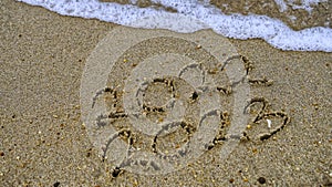 Photo of coming New Year 2023 and leaving year of 2022, Wrote text on sand at some beach with the small ocean wave.