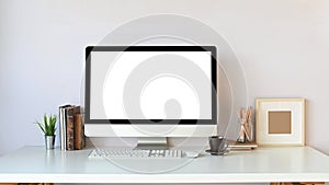 Photo of Computer monitor with white blank screen, stack of books, potted plant and wireless keyboard.