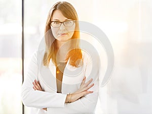 Portrait of confident businesswoman standing with arms crossed at office and yellow lens flare in background