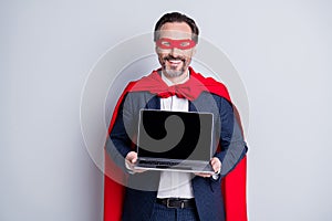 Photo of confident cheerful aged mature business guy super hero costume hold laptop presenting novelty new device model