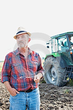 Confident senior farmer standing against mature famer driving tractor in field photo