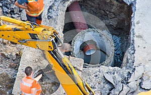 Photo of construction or active repair water supply, sewer or pipe drainage system in concrete pit by workers in orange vests with