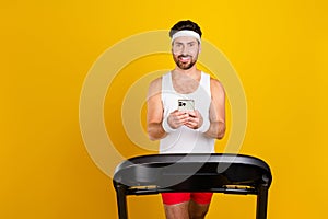 Photo of cool cheerful guy activewear walking treadmill texting apple iphone samsung gadget empty space isolated yellow