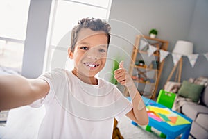 Photo of cool confident small boy wear white t-shirt recording video vlog thumb up indoors room home house