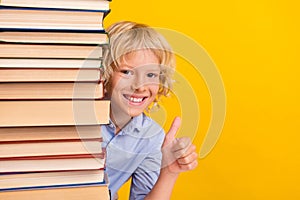 Photo of cool little boy thumb up near books wear blue shirt isolated on yellow color background