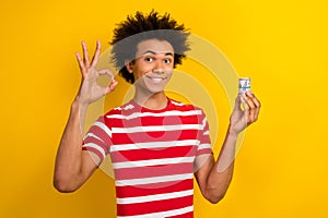 Photo of cool positive guy wear striped t-shirt showing okey showing money cash roll isolated yellow color background