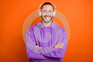 Photo of cool young brown tail hairdo guy crossed arms listen music wear purple hoodie isolated on orange color